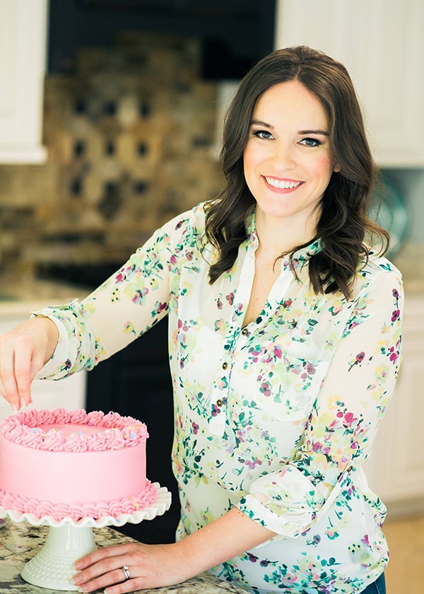 lindsay standing in a kitchen putting sprinkles onto a pink cake